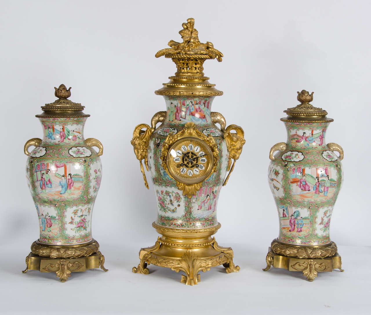 A very decorative Chinese canton porcelain and French ormolu-mounted clock garniture, having a pair of vases either side of the clock. The mounts to the clock with scrolling foliage and ram's heads.