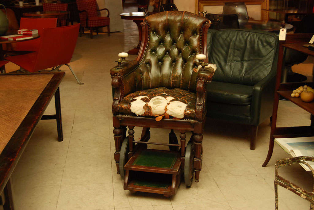 Unique original wheel chair, early Victorian, in dark green tufted leather, with porcelain and brass levers which turn chair in different directions.  Manufacturer's label 'J Ward Manufacturer to the Royal Family'.  Carved and scrolled arms and