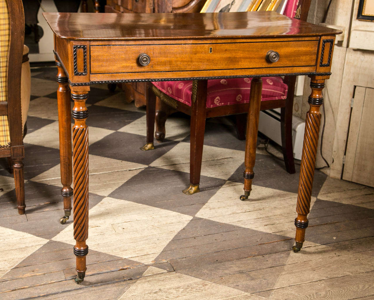 A beautiful pair of faux drawer front side tables in light colored mahogany.  Spiral twisted legs  ending in brass casters.  Black painted  decoration to tops  and  bottoms of leg  rings,  flanking the  faux  drawers, and along the lower edge. The