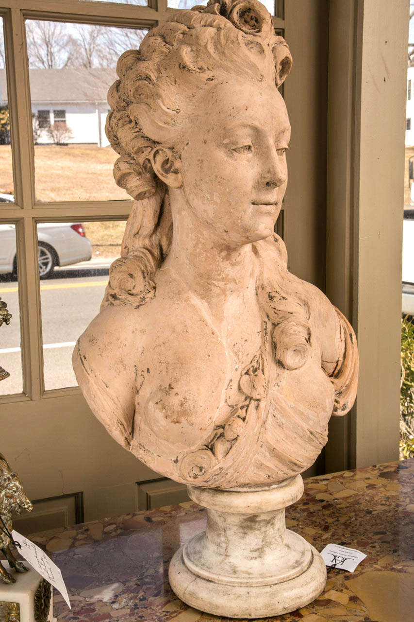This bust of  Mme. DuBarry(?) is signed Caffieri and dated 1790. Her eyes  lok to the left and over her left shoulder, a cascade of curls hangs to her breast. Long curls hang down the back of her head in the style of the 18th century. Raised  on a 