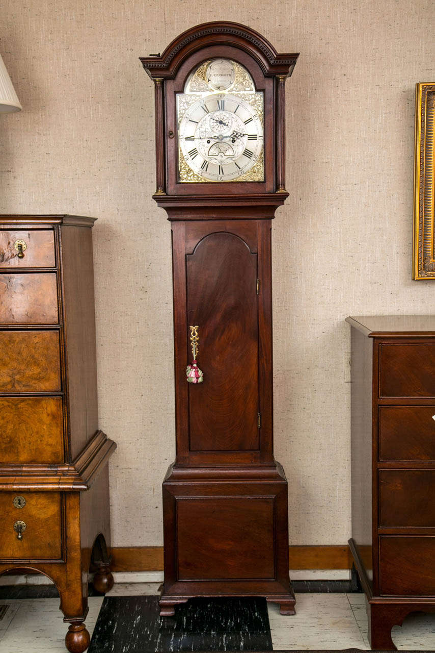A domed and dentil moulded bonnet with side colonettes frames a brass and silvered brass dial with chinoiserie engraved steel center surrounded by cast brass spandrels on this attractive tall case clock. The case has an arch top door leading down to