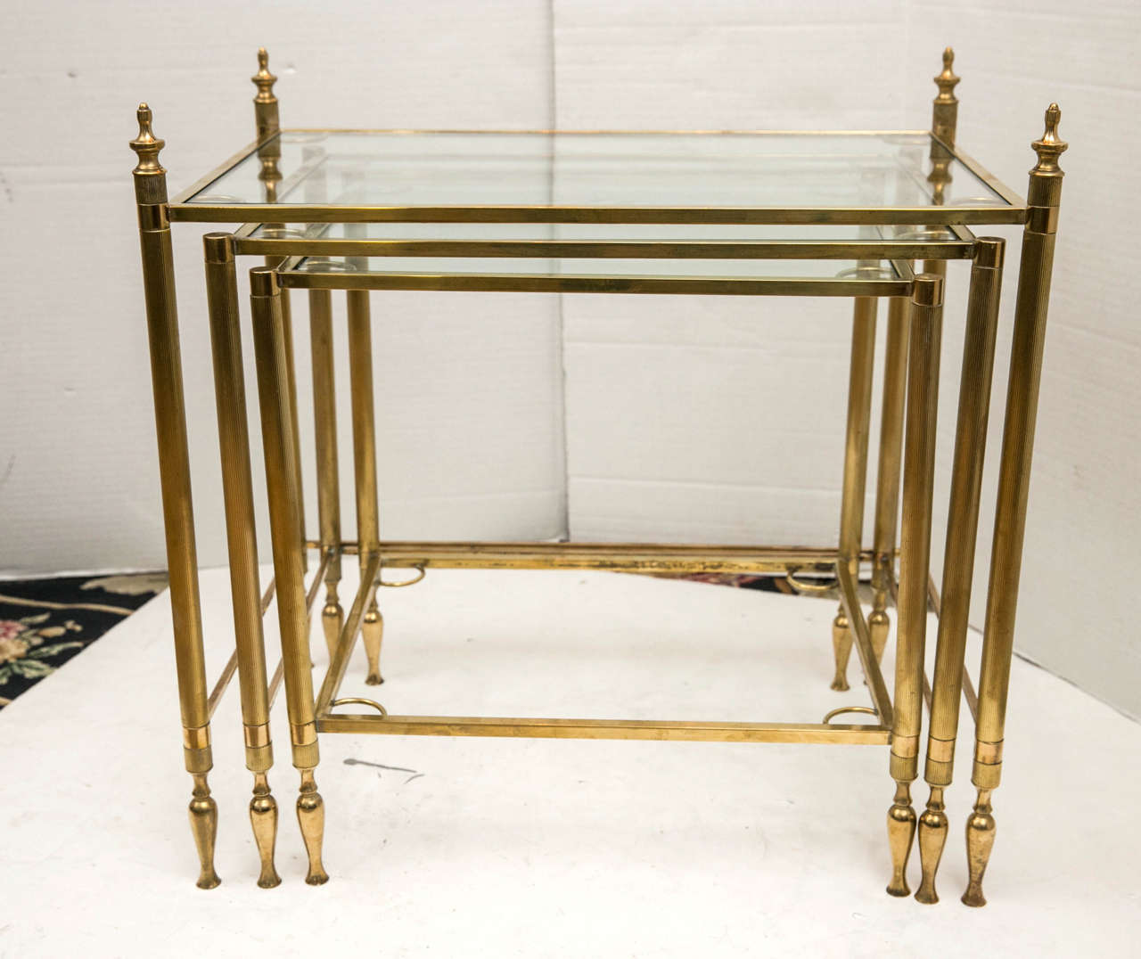 A set of three polished brass frame nesting tables with glass tops. The smallest table has a lower glass shelf.