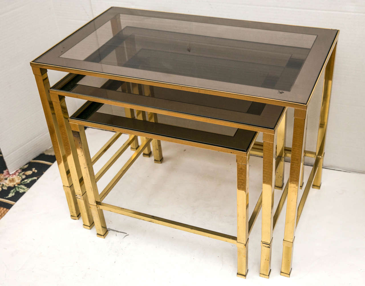 A Set of three Mid-century french nesting tables. The bases are polished brass, and the glass tops feature smoked glass edges.