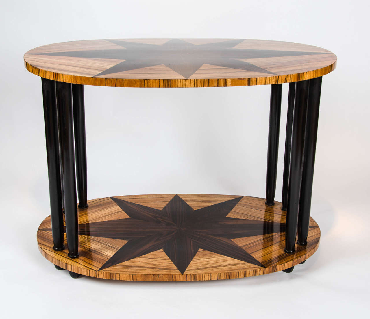 An Art Deco oval side table in palisander wood with macassar ebony star shaped inset. Top set on ebonised wood straight column legs over a lower shelf on ebonised feet.