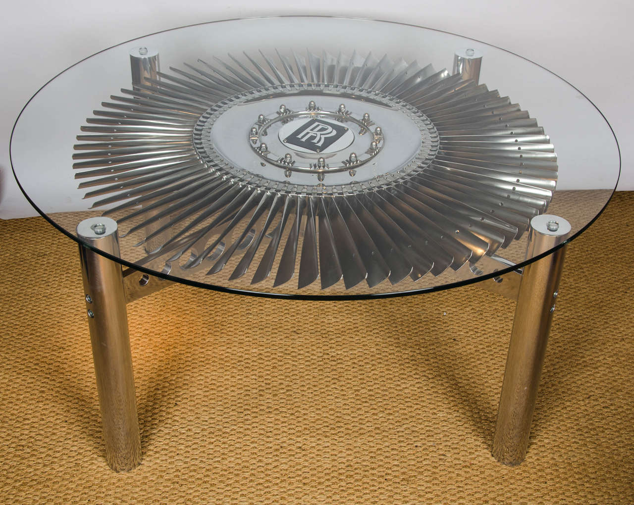 A Rolls Royce turbine, metal and glass coffee table. Made using the cleaned and repolished turbine blades from a Rolls Royce Pegasus engine used in the Hawker Harrier (Jump Jet).  The turbine blade is mounted on a smooth running bearing and rotates