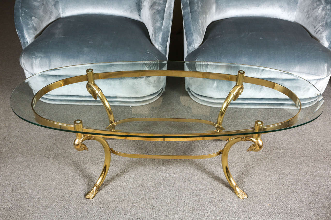 Lovely oval coffee table with a graceful polished brass base with goose heads and webbed feet. The table has an oval glass top.