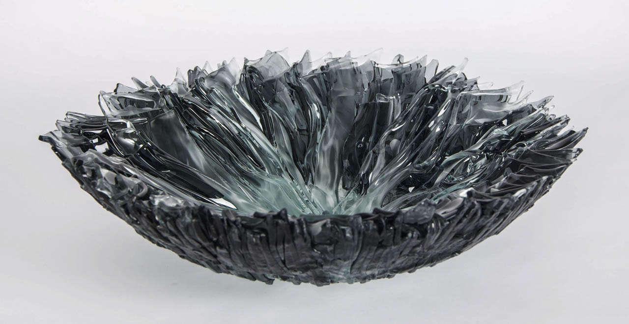 For charmer the draw of glass is to exploit its translucent and reflective qualities. His bloom bowl series are constructed from numerous hand cut-glass shards. Whilst heated for several days in the kiln, the sharp edges are softened resulting in
