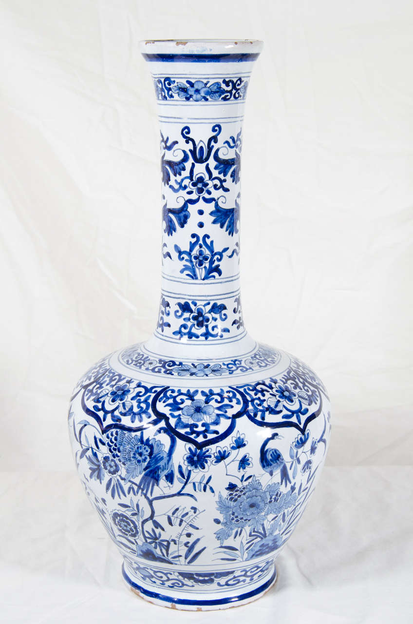 A pair of Dutch Delft blue and white bottle vases decorated in cobalt blue with scenes of peacocks and long tailed birds among peonies. Above and below the scenes are bands of scrolling vines, leaves and flowers.