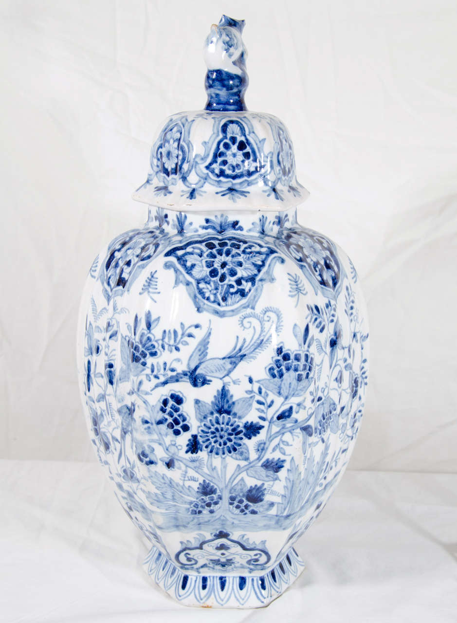 A pair of hexagonal Dutch delft covered vases painted in soft tones of cobalt blue decorated with  a scene of long tailed birds among peonies and bands of lambrequins, rui and long leaves. The covers topped with traditional lion finials.
