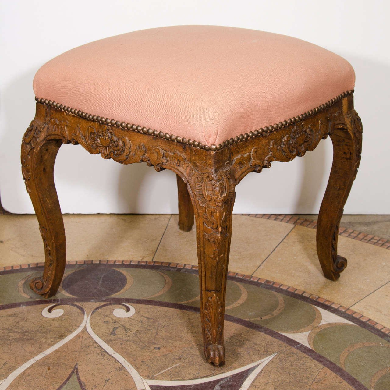 A Louis XV carved oak stool with foliate motifs and cabriole legs ending in scroll feet.