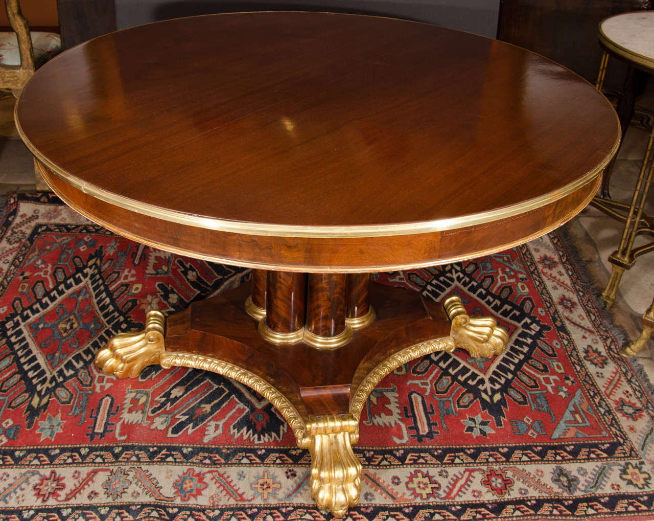 A Regency mahogany center table with brass banded rim and gilt moldings raised on a cluster column pedestal ending in gilt paw feet.