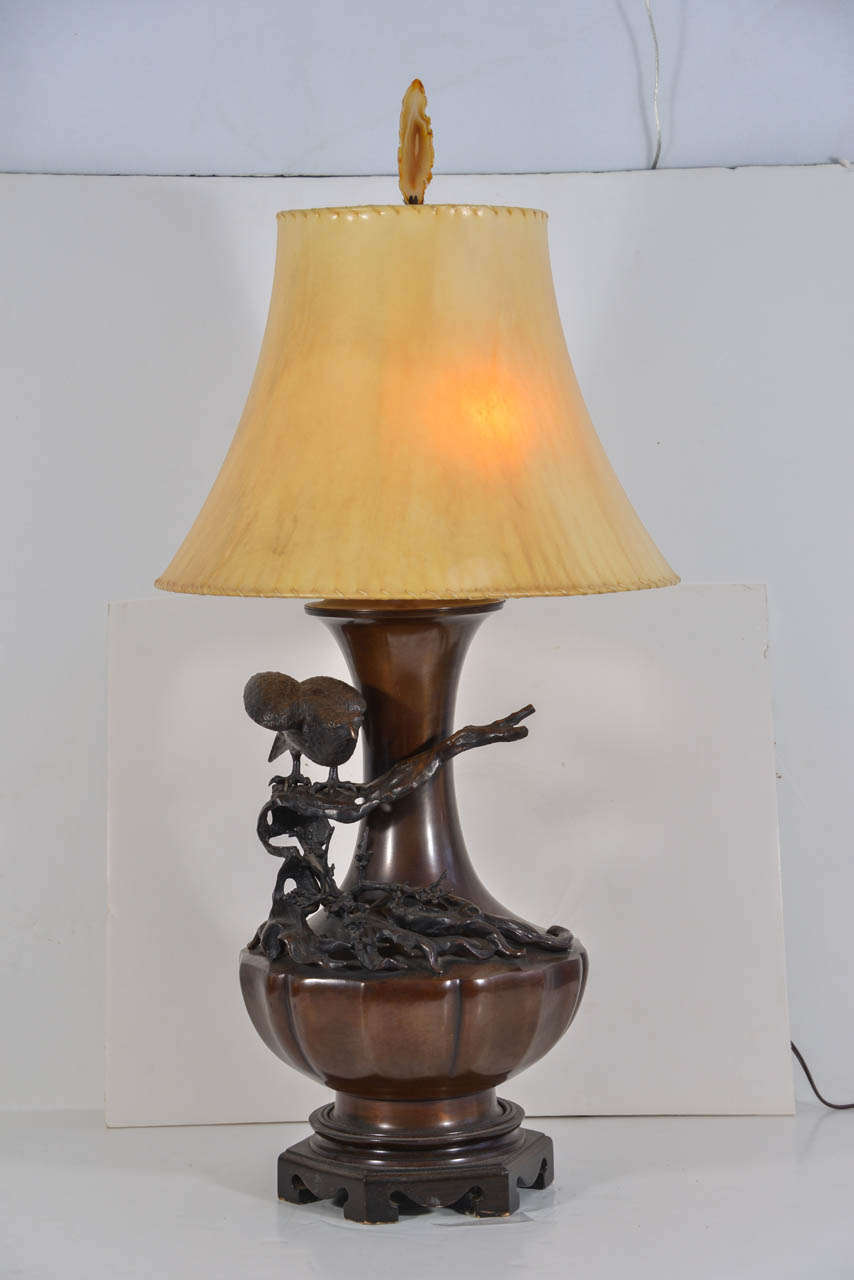 Cast bronze table lamp with cast bronze bird on a branch ornamentation. Features a custom-made sheep skin lamp shade and finial made of a slice of geode. Lamp is priced without shade and finial. Shade is $350 and finial is $45.00.