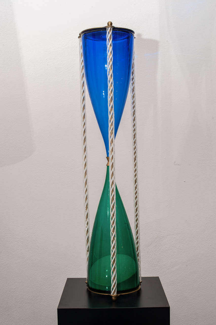 Large hour glass: blue and green glass, staffs with lattimo sphirals, brass mounting.
Designed by Paolo Venini. Murano, circa 1950.
Edition of 1994, n. 2 of 9.
Engraved signature: venini 94/2/9.