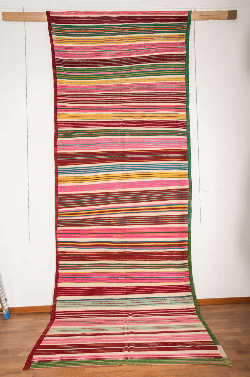 A colorful Tunisian Kilim decorated by a repeat pattern of horizontal stripes arranged in clusters of different width and palette. A very happy piece celebrating the arrival of Spring!