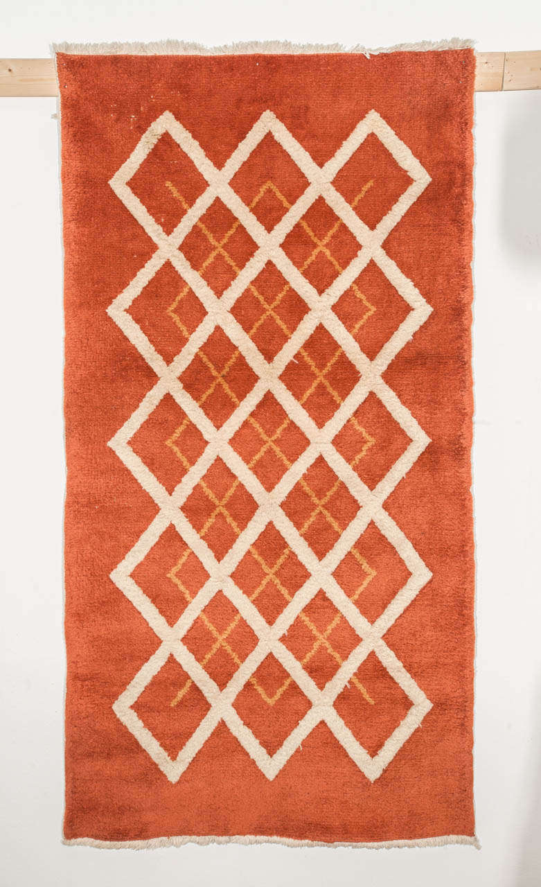An Art Deco rug distinguished by a repeat pattern of honey-arranged ivory lozenges knotted with a raised pile, contrasting with a similarly arranged cluster of apricot lozenges woven at the same height of the orange background.
The rigorous geometry