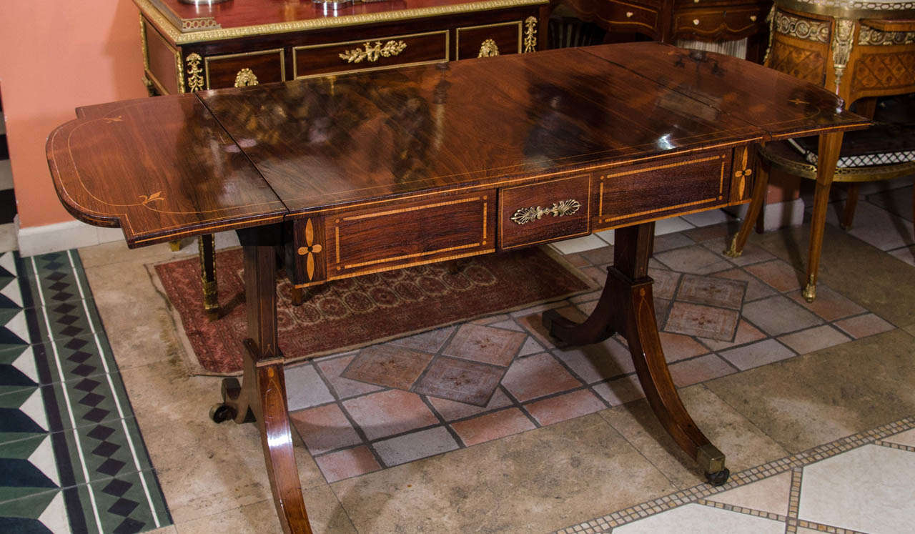 A Fine Regency rosewood drop leaf satinwood sofa table with trestle ends and brass caster feet.