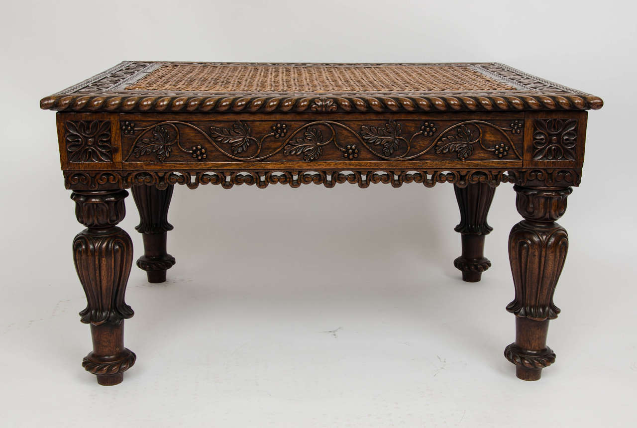 An early 19th century Anglo-Indian heavily carved stool with caned seat.