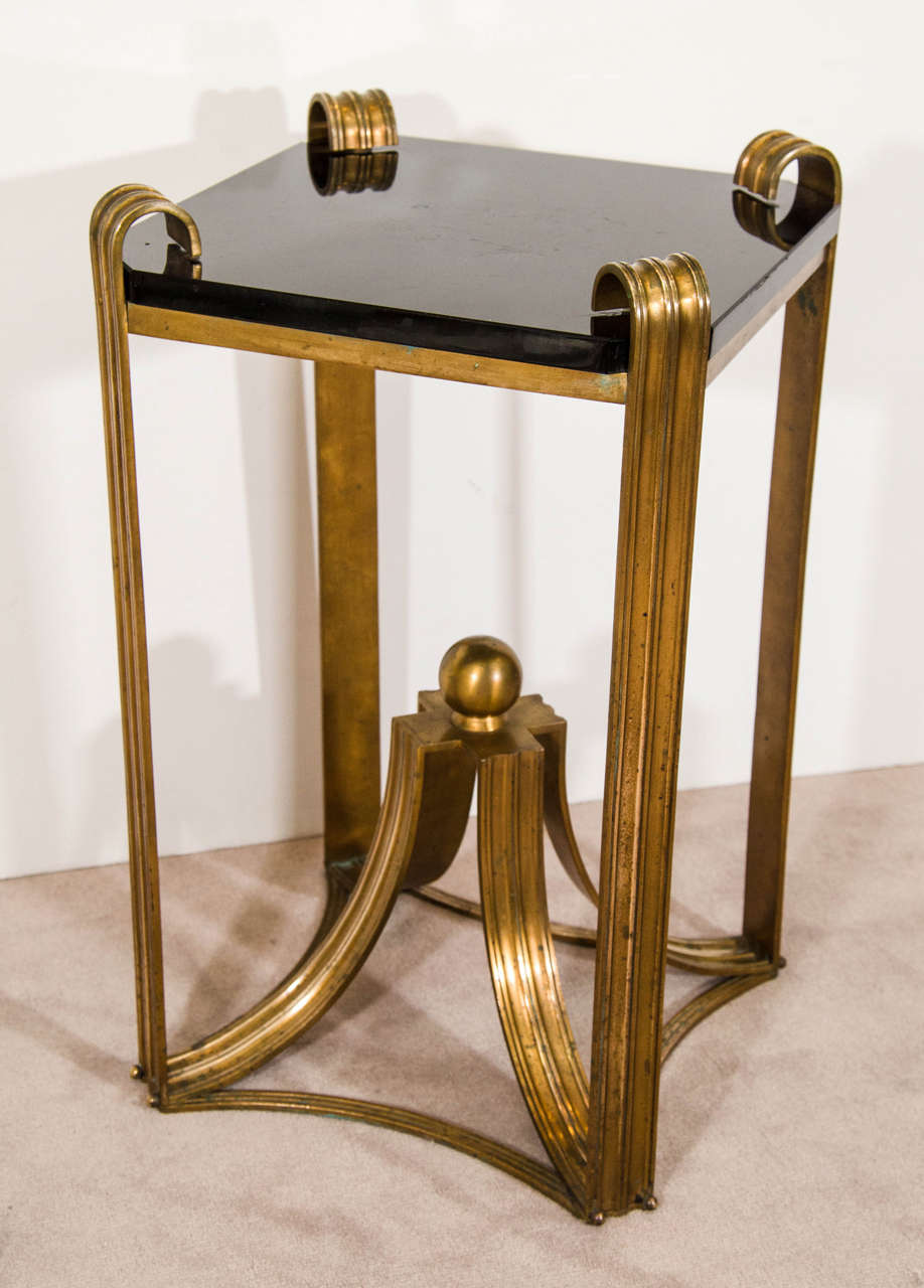 A vintage pair of Art Deco moderne side tables, circa 1930s with curved bronze design and center bronze ball. The thick black glass top is reminiscent of Raymond Subes. Good vintage condition with age appropriate patina. Some pitting and light