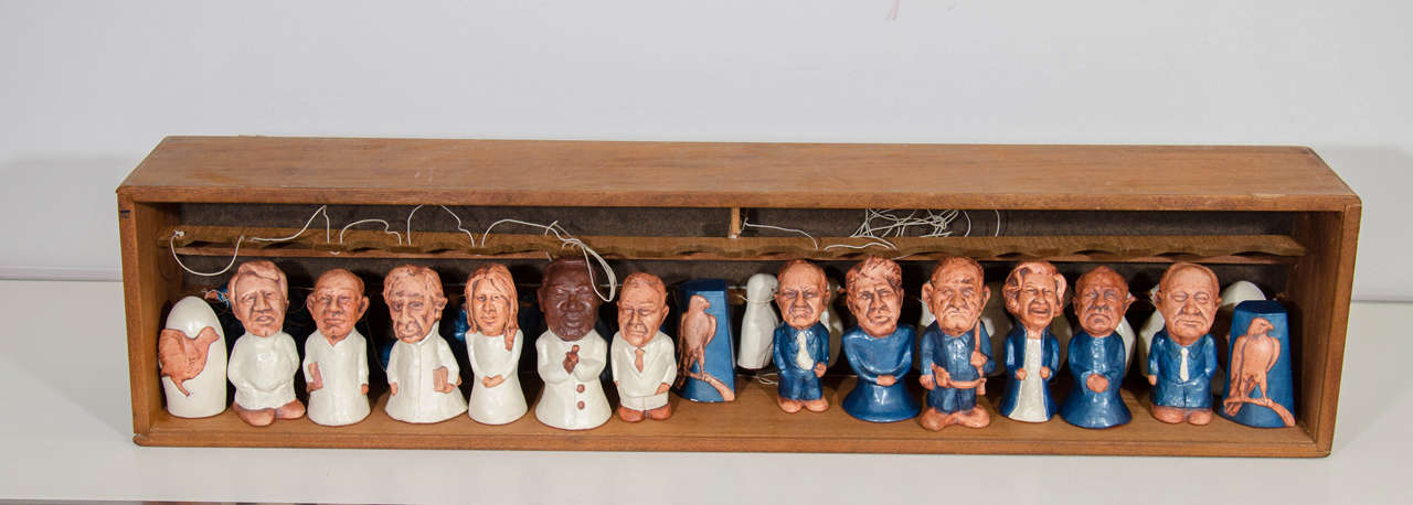 A vintage set of chess pieces in a wooden storage box by New York Artist Myrna Goldberg. The chess pieces are figures of politicians, activists, and others who played a significant role in 1960s. The glass lid is labeled with each name and is signed