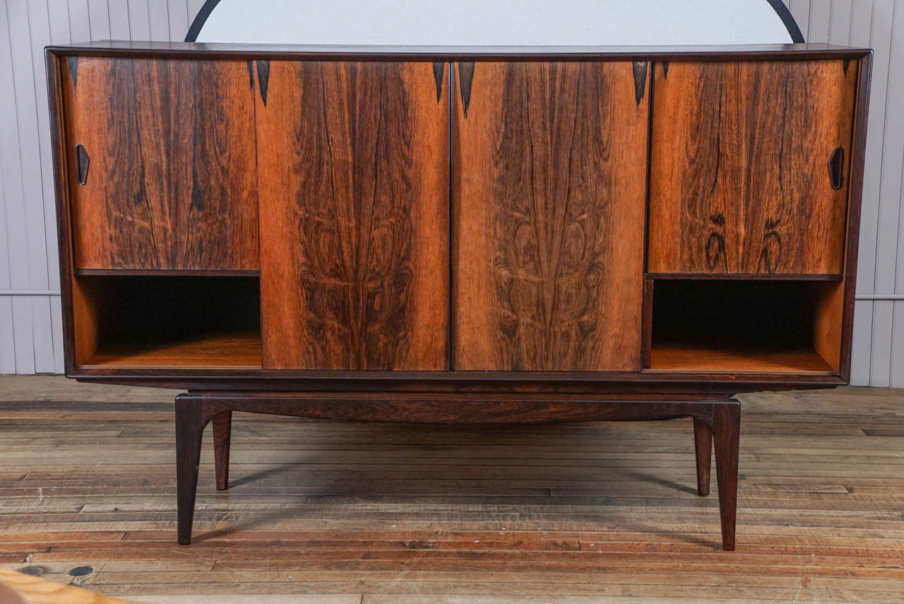 Stoic Danish modern credenza in rosewood, four sliding doors, center section composed of six drawers and shelves, end compartments each contain one adjustable shelf resting on ebonized wood base.