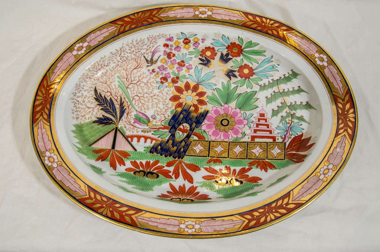 This large Barr Flight Barr Worcester platter shows a lovely English interpretation of a Chinese landscape scene with a pagoda, flowering trees and longtailed birds. Beginning with Imari colors Worcester added Famille Rose pastels to create this