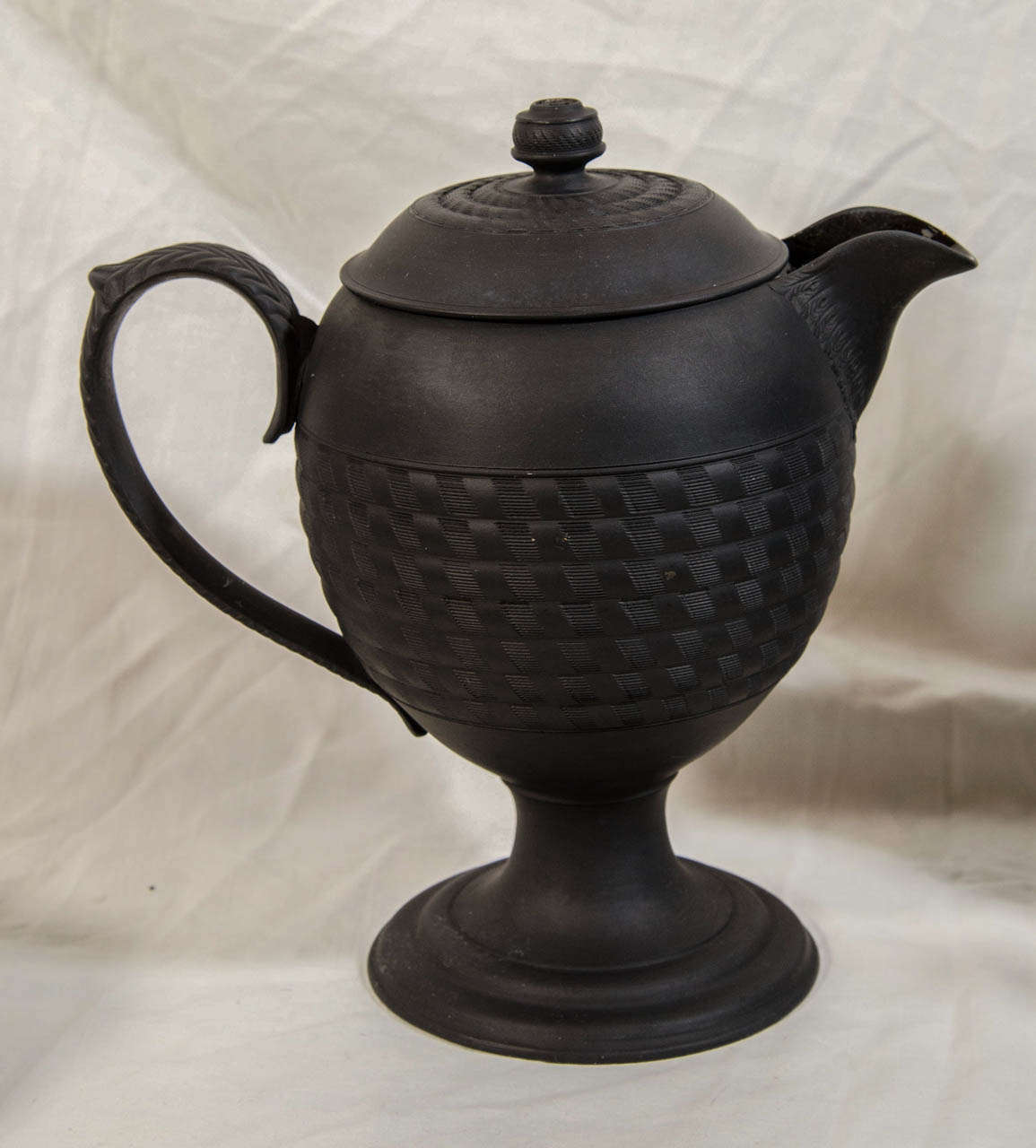 A group of early 19th century engine turned Black Basalt wares comprising a cylindrical teapot and cover modeled with classical figures, and three coffee pots with machine turned architectural details. Black basalt was introduced by Josiah Wedgwood