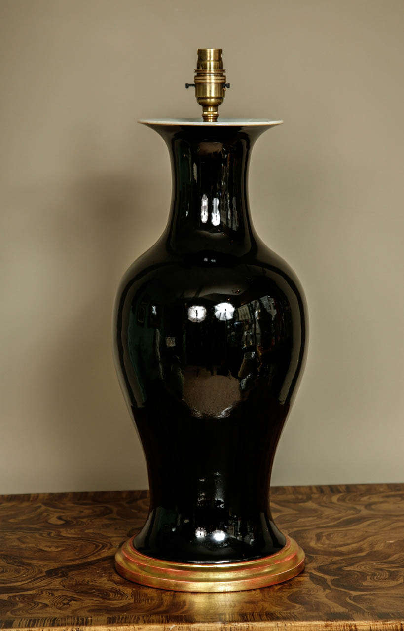 A large Chinese mirror black glaze baluster vase. Good thick reflective black glaze to the exterior, the flaring rim with internal white glaze. Good solid colour, late 18th-early 19th century porcelain. On a hand carved water gilt wooden base and