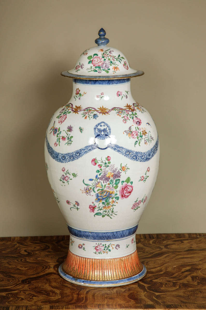 A large Chinese porcelain Famille Rose baluster vase and cover ca. 1775. Decorated in exquisite flowers and blue & white swags. The vase as a flared foot decorated with iron red and gilt panels.  The shoulder is decorated with floral bands. With