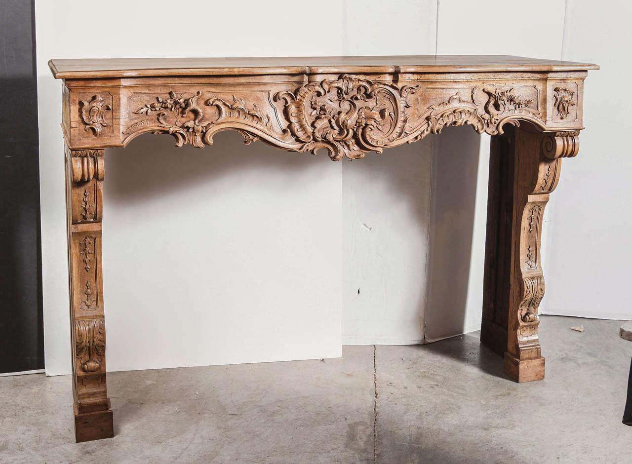 This superb antique French walnut wood mantel is from a home in Marseille and is in the Regence Style.

The French walnut wood has been stripped at one point in its history.  The hand carved motifs are absolutely stunning!  Scrolling rinceau and