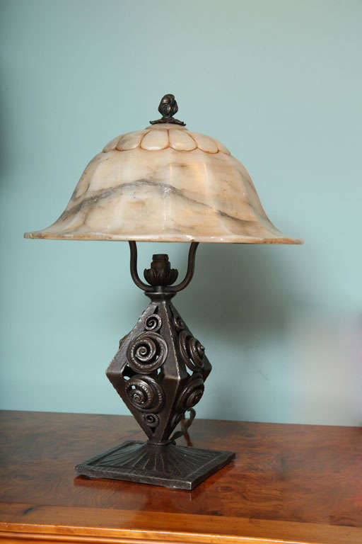 A French Art Deco Wrought Iron and Alabaster desk lamp decorated with classic bell shaped alabaster a top a highly stylized Art Deco wrought Iron lamp base.