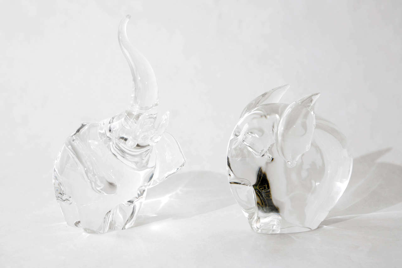 A charming duo of crystal elephants by Steuben Glass. The trumpeting elephant on the left was designed in 1964 by glass artist James Houston. The elephant on the right was designed in 1960 by glass artist George Thompson. Dimensions given below are