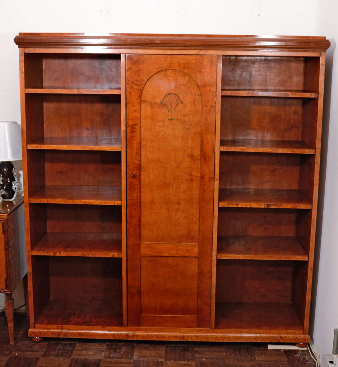 A centre door divides this bookcase into a pair of open display areas, flanking a locking area for private books and artefacts. The neoclassic fan motif of mahogany, birch and ash, is prominently displayed below the arched inset door panel.