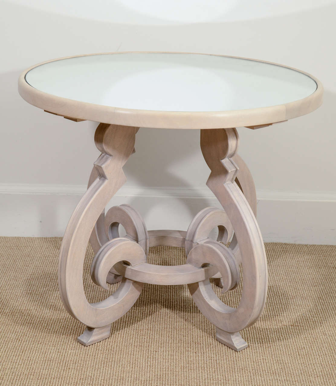 The circular topped table supporting a mirror, raised on four scrolling legs, lined by a circle.