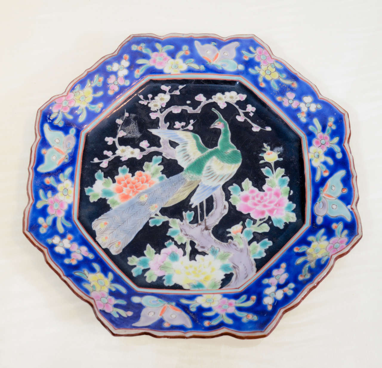 Eight-sided famille noir porcelain plate depicting peacock with blue and pastel decorated border.