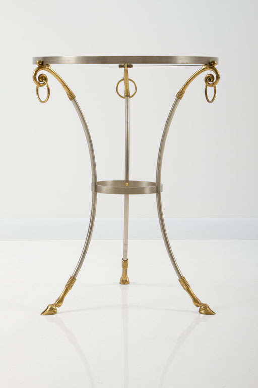 A finely detailed guéridon table with an inset glass top in a satin steel frame with bronze cloven hoofs and bronze mounts. Stamped tag [Made in Italy]. Italy, circa 1960.