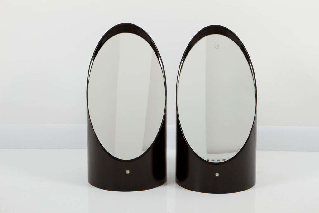A Post Modern pair of vanity mirrors comprising black resin casings with inset elliptical mirrored glass. Maker's mark to each base. France, circa 1970.