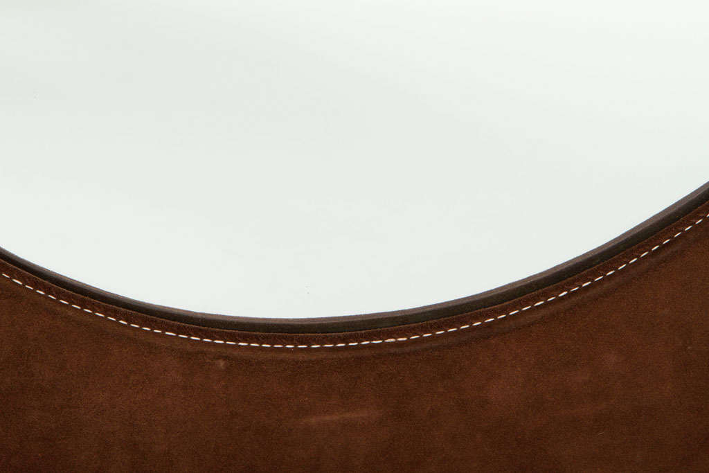 A chic wall mount mirror wrapped in chocolate brown suede with saddle stitched edges, in a rectangular frame with a circular mirror. After Pierre Cardin. American, circa 1970.

