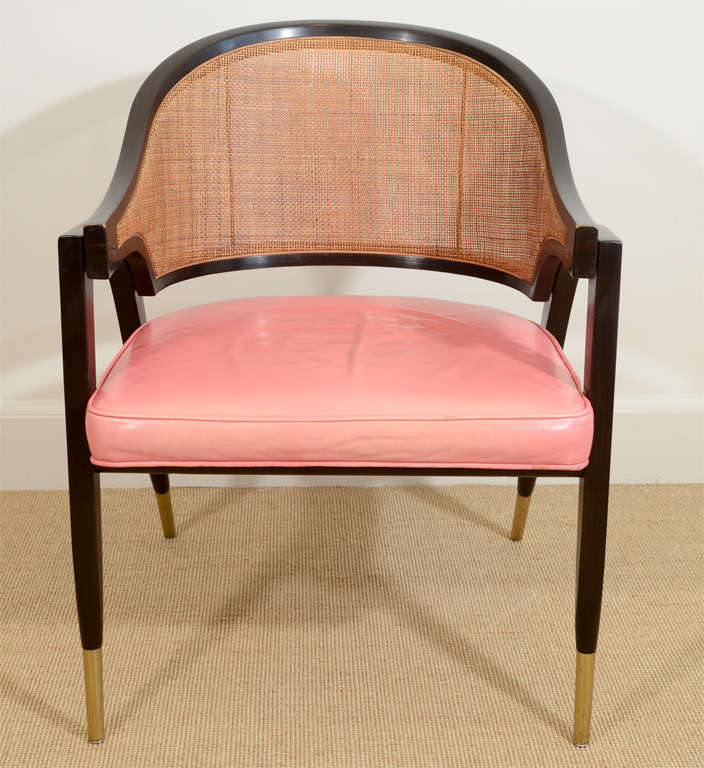 The curved cane backed and sides, with tapering angled legs with brass sabots, supporting a pink leather seat.