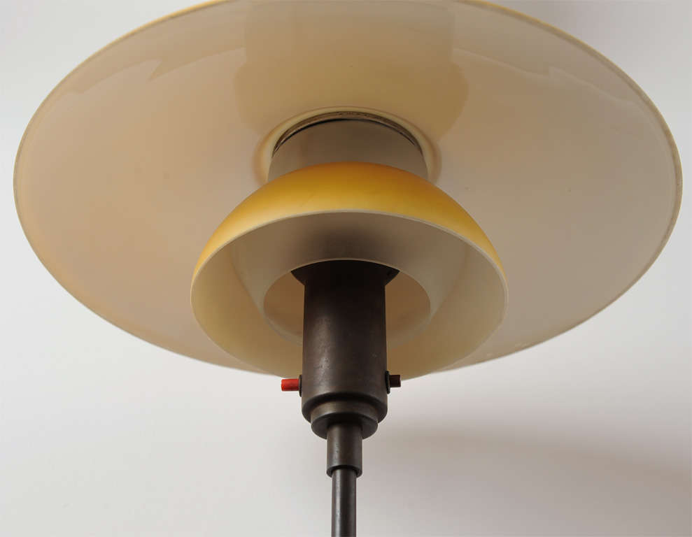 Browned table lamp with power switch in the socket housing, top- and middle shade of yellow painted opal glass, bottom shade of frosted glass.