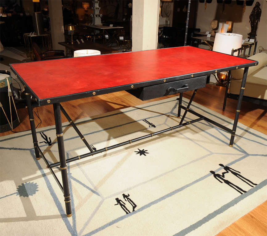 An exceptional faux-bamboo, black lacquered metal and brass trimmed desk with original red-leather top by Jacques ADNET (1900-1984)  The top edge leather-wrapped metal, fitted with a black leather drawer.
France - circa 1950