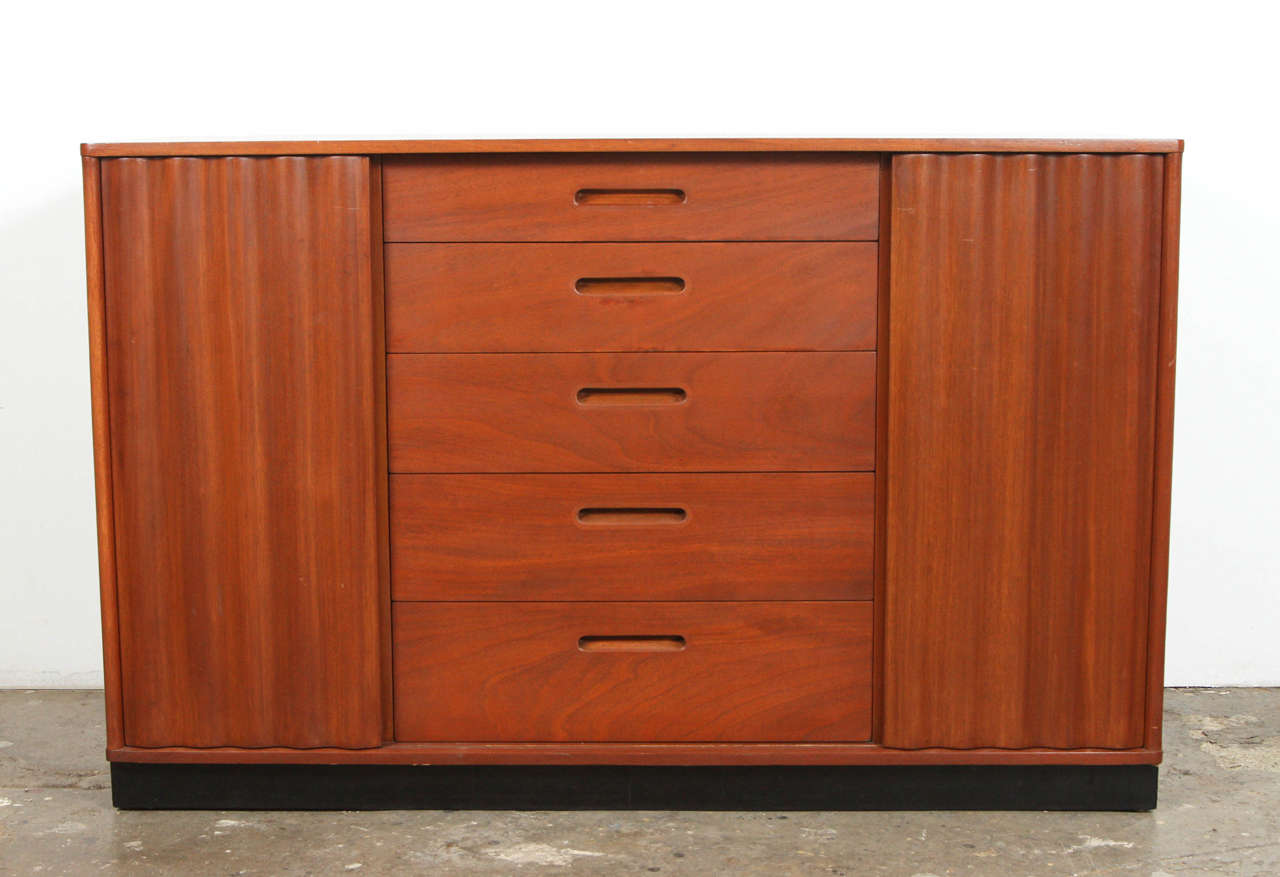 Mid-Century Dunbar cabinet with corrugated wood front. Beautiful, well designed piece, corrugated slide wood doors to hide center drawers and then reveal side shelving. Original Dunbar stamp under drawer. Newly refinished in a light brown. While