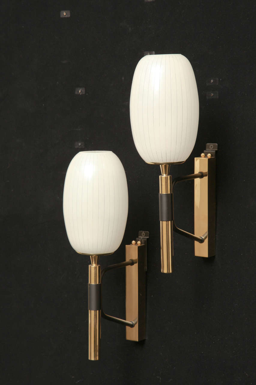 Pair of Polished Brass One Light Sconces With Polychrome Support Mounts.
The Opaline Glass Shades Are Oval Shaped With Clear Lines Spaced Evenly Around The Shade.