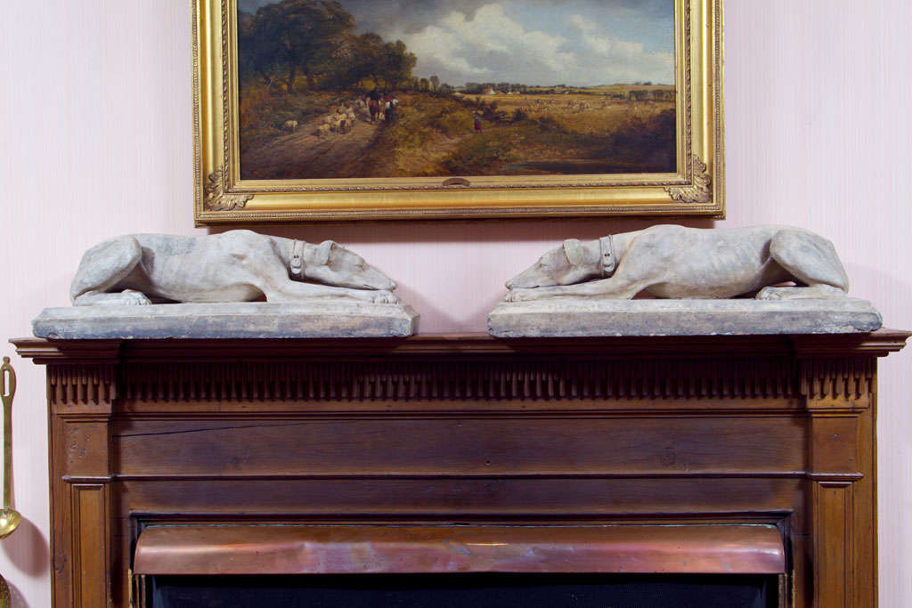A rare pair of recumbent Coade stone greyhounds, each wearing a collar with clasp and lying with tail tucked under, on integral plinth base having an impressed mark 