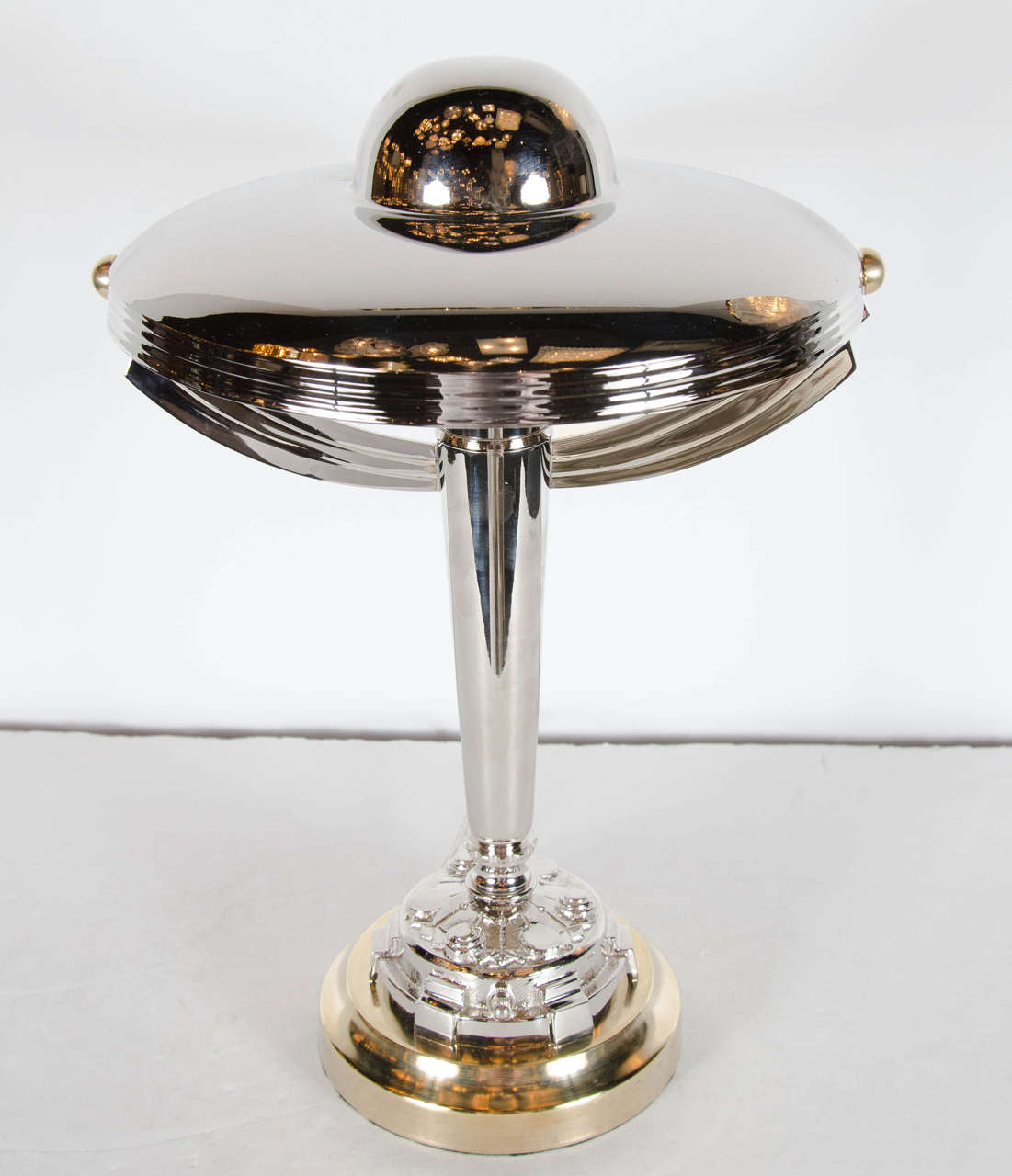 This stunning desk lamp is made of polished nickel and brass. It features a streamline design with stepped supporting arms supporting a domed shade . The base features a stylized geometric Art Deco design on the base. The lamp has been completely