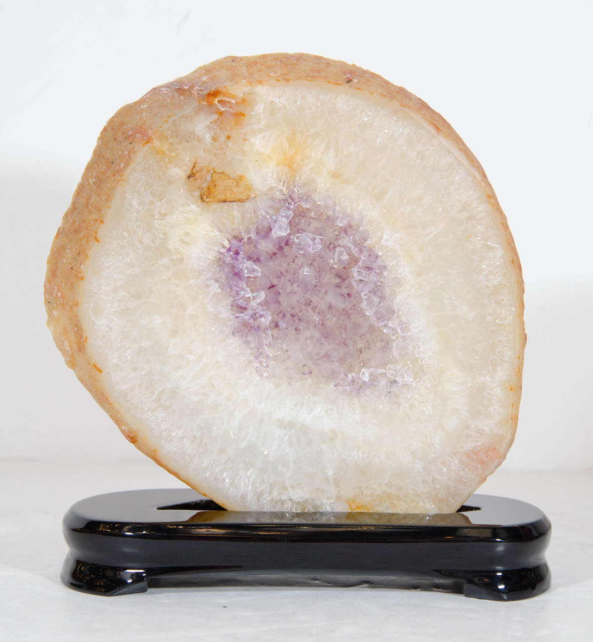 This sliced geode, with its honeyed exterior, crystalline ecru perimeter and lilac amethyst center, is absolutely stunning. It sits on an elegant ebonized walnut base. The simple circular form and subtle palate ensures that it will blend seamlessly