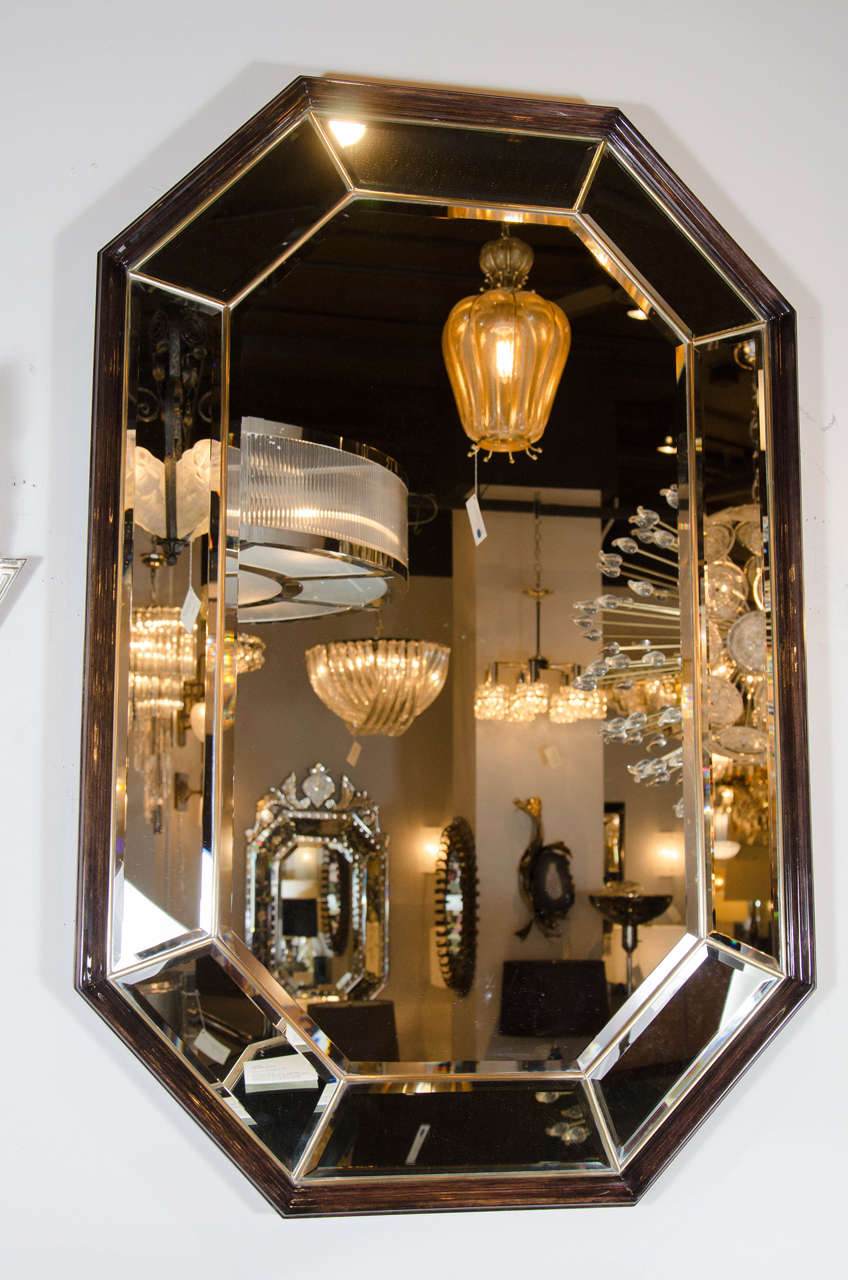 This sensational Mid-Century modernist octagon form mirror is a one of a kind. This piece has an elegant and sophisticated design with ebonized walnut detailing, inset brass trim and beveled detailing on all the mirrored panels. It is in excellent