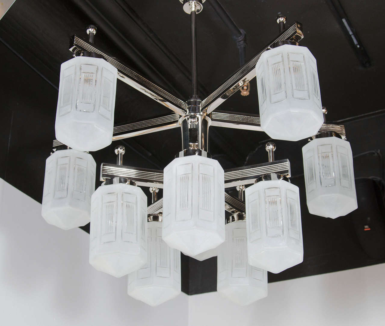 This graphic and elegant Art Deco style chandelier in polished nickel features ten arms attached to an angular geometric frame and nine relief etched frosted glass globes with intricate rectilinear concentric detailing. With its monochromatic palate