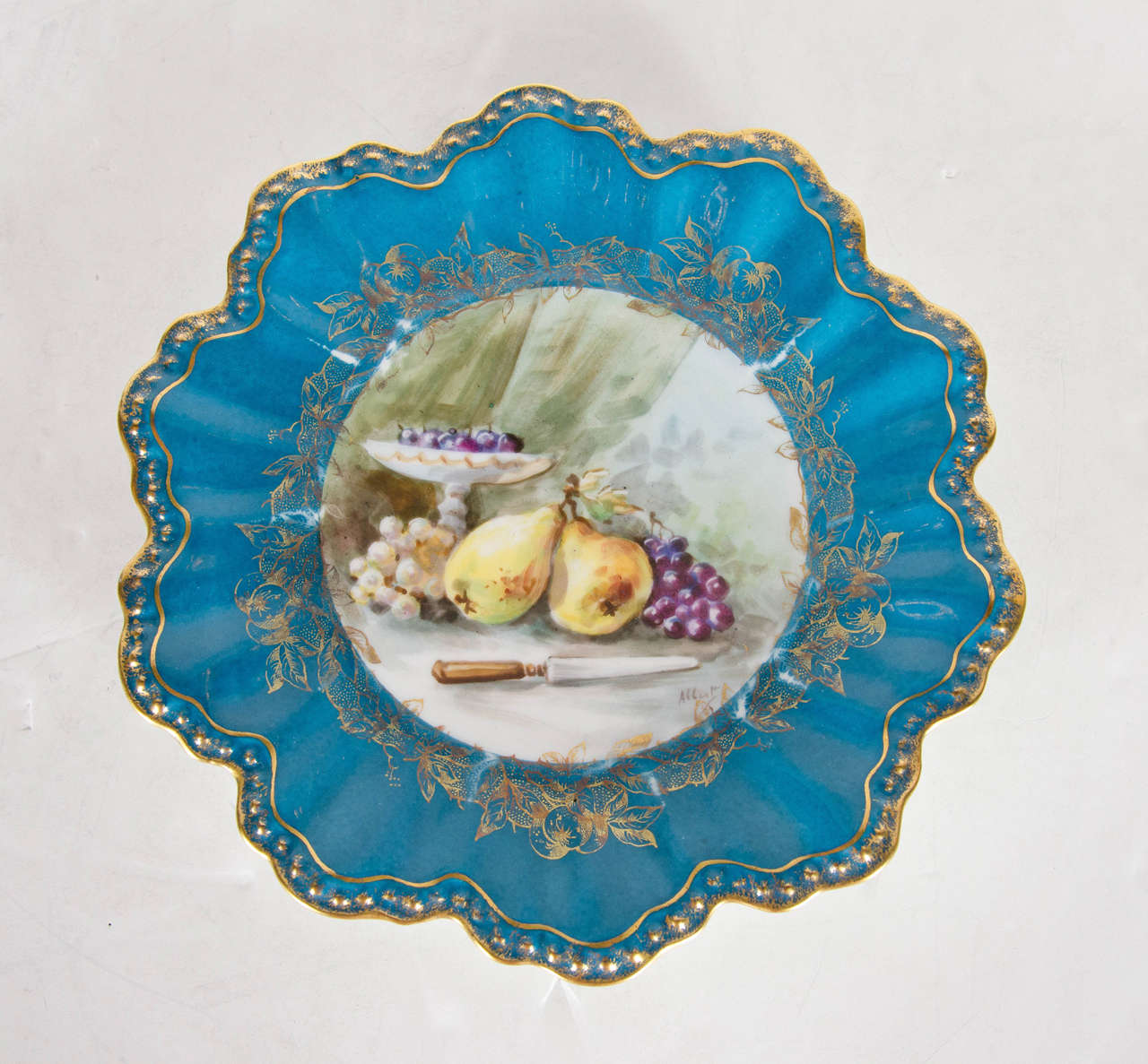 This elegant set of 12 hand-painted desert plates features a scalloped edge gilded with 24-karat yellow gold. The centre of each plate has been painted with a different realist still life. One features apples, a water carafe and glass, and a bread