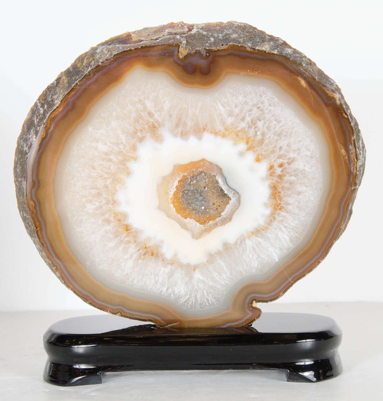 This stunning sliced geode agate features a circular design with three interior layers of vibrant colors. Mixed in shades of citrine, pearl, and umber it's uniqueness is a one of kind. In the center of it's cylindrical shape, there is an amassed