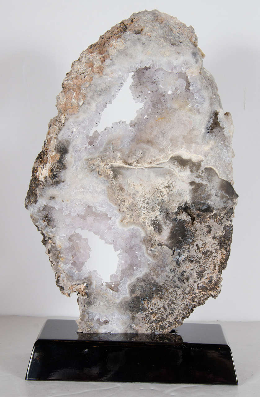 This gorgeous sliced geode crystal specimen features multiple shades of grey. It's oval form gives the geode added dimension, while the interior quartz crystals show it's vibrant detail. It would look spectacular in any room or decor and rests on an